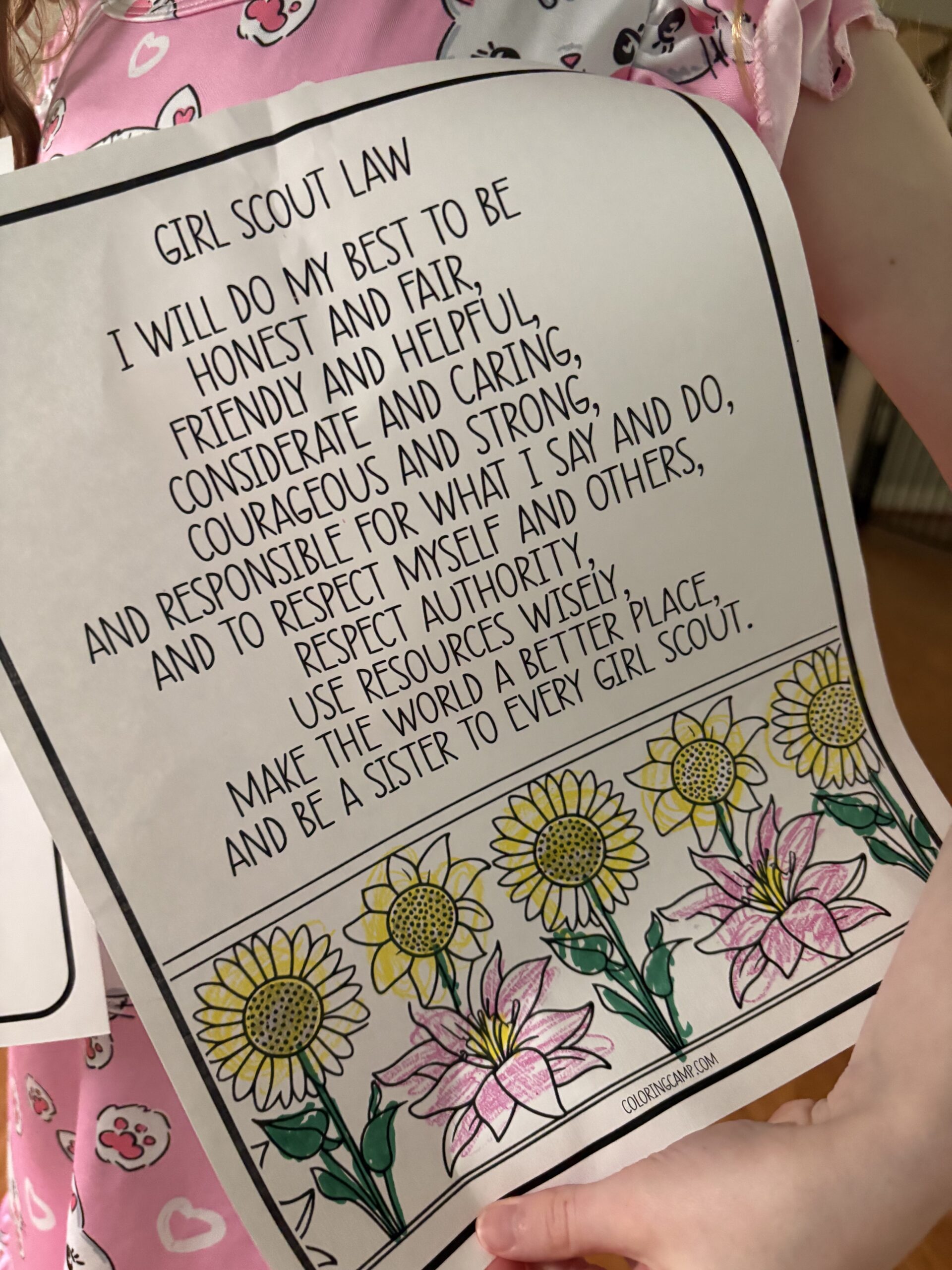 A young girl holding a Girl Scout Law coloring page with flowers.