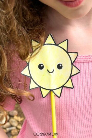 A child holding a summer wand craft (a sunshine template on a paper straw).
