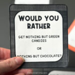 A hand holding one of the Halloween would you rather questions.