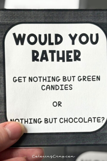 A hand holding one of the Halloween would you rather questions.