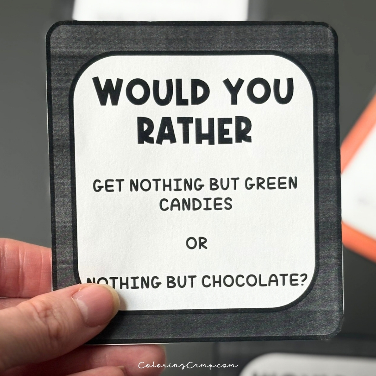 A hand holding one of the Halloween would you rather questions.