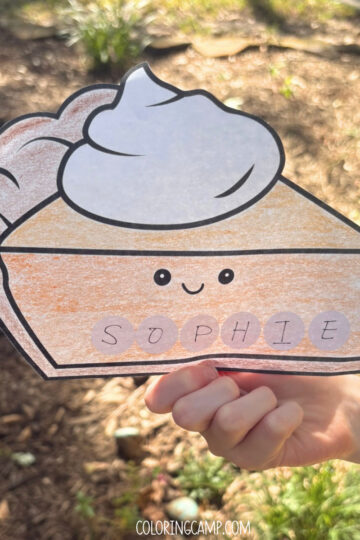 A child's hand holding a Thanksgiving name craft that spells "Sophie."
