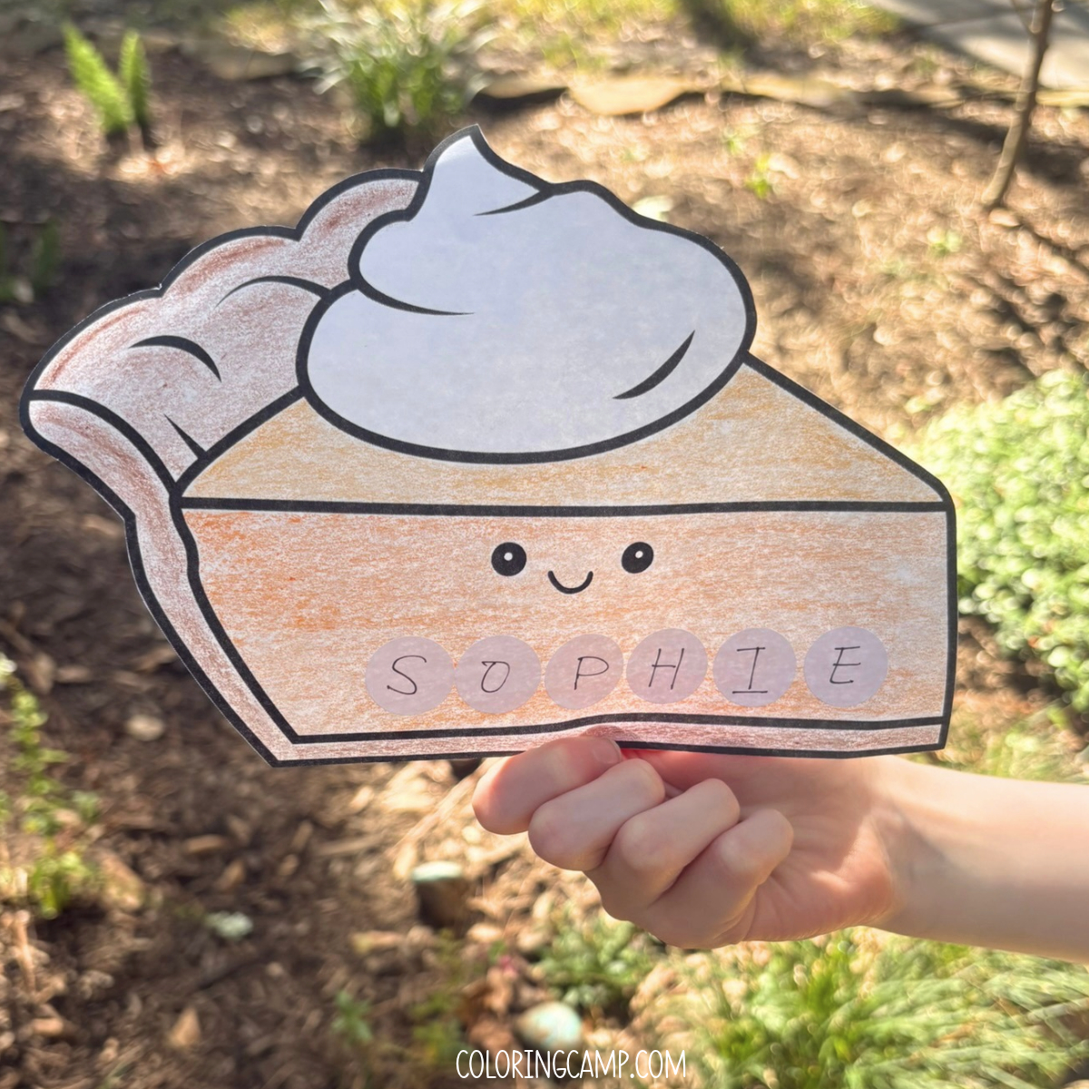 A child's hand holding a Thanksgiving name craft that spells "Sophie."